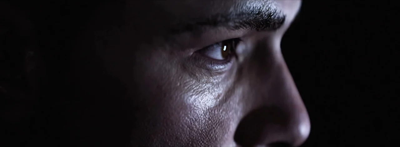 Extreme close-up of a man's face in profile, half-lit and half hidden in shadow during a cutscene